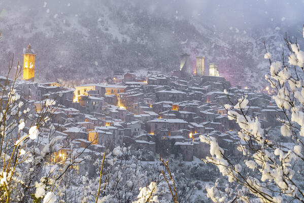 Dusk in the illuminated medieval village of Pacentro seen from below under heavy snowfall  with the castle and bell tower in the background and snow covered house, Pacentro municipality, Maiella national park, L’aquila province, Abruzzo, Italy
