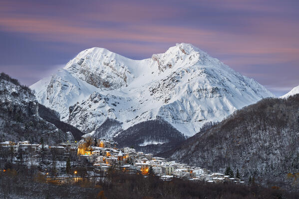 Winter dusk in the snowy illuminated mountain village of Pietracamela with the majestic Intermesoli peak in the background, Gran Sasso and Monti della Laga national park, Teramo province, Abruzzo, Italy