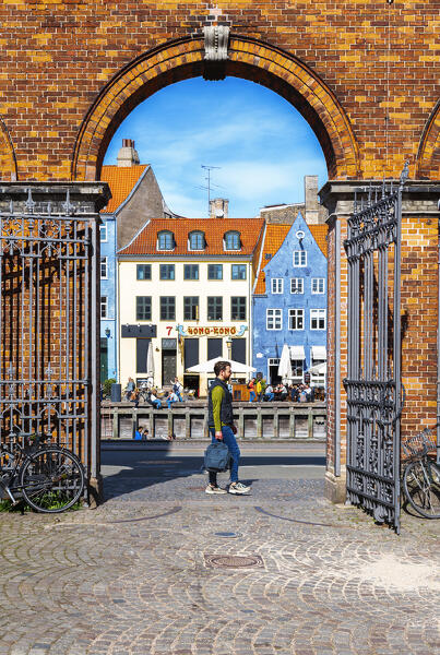 View of the man walking in the street of the colourful buildings of Nyhavn district seen throught an arch made by bricks, Copenhagen, Hovedstaden Denmark, Europe