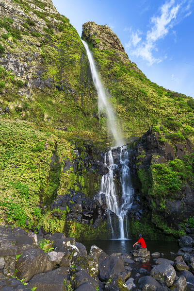 Man admiring the waterfall of Poco do Bacalhau at the sun light in Faja Grande, Lajes das Flores municipality, Flores Island (Ilha das Flores), Azores archipelago, Portugal, Europe