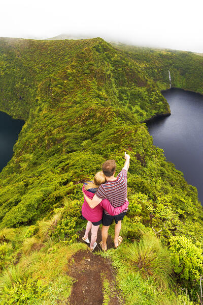 Rear view of a man and woman admiring the beauty of the Lagoa Negra e Lagoa Comprida caldera, Miradouro Lagoa Negra e Lagoa Comprida, Reserva Florestal Natural Morro Alto e Pico da Se, Lajes das Flores municipality, Flores Island (Ilha das Flores), Azores archipelago, Portugal, Europe