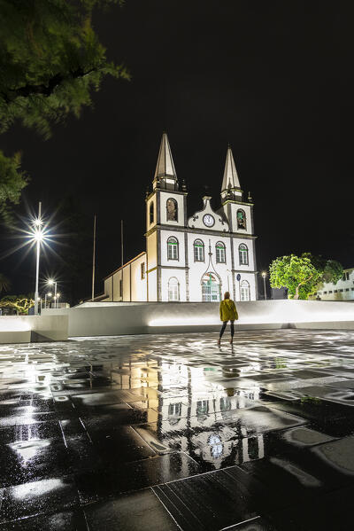 Woman standing in the night in front of the illuminated igreja de Santa Maria Madalena  with reflection, Madalena municipality, Pico island (Ilha do Pico), Azores archipelago, Portugal, Europe (MR)