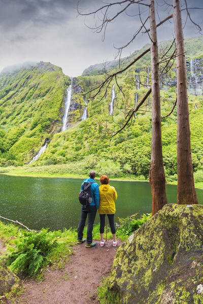 Rear view of a man and woman admiring the beauty of the waterfall of Ribeira do Ferreiro, Poco Ribeira do Ferreiro (Alagoinha), Lajes das Flores municipality, Flores Island (Ilha das Flores), Azores archipelago, Portugal, Europe