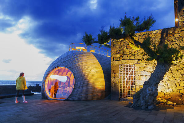 Woman standing in front of an exclusive cafe with reflection at dusk, Madalena, Madalena municipality, Pico island (Ilha do Pico), Azores archipelago, Portugal, Europe