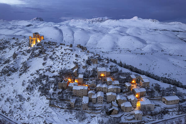 The illuminated medieval village and the castle of Rocca Calascio covered with snow  at dusk, winter aerial view, Rocca Calascio, Gran Sasso e Monti della Laga National Park, Apennines, L'Aquila province, Abruzzo region, central Italy, Italy, Europe