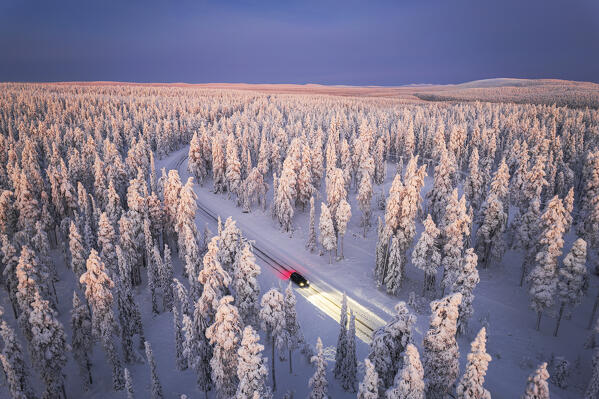 Car traveling on icy road crossing the winter forest covered with snow from above, Lapland, Finland, Scandinavia, Europe
