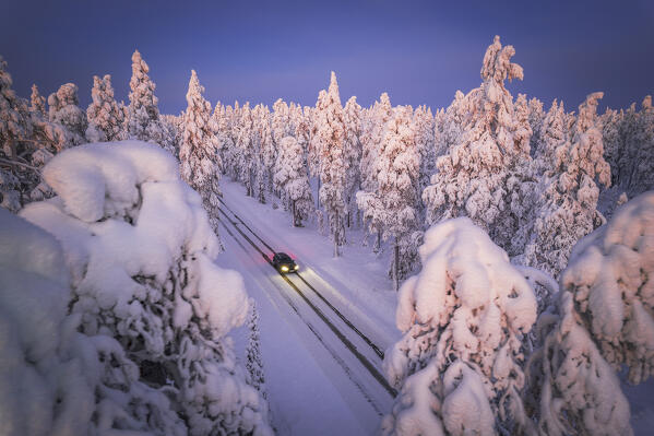 Drone view of a car with headlight on travelling the icy slippery road crossing the forest covered with snow, Muonio, Lapland, Finland, Scandinavia, Europe
