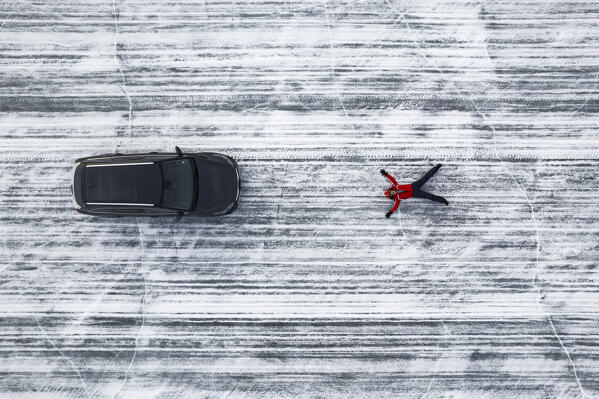 Aerial view of a happy person with open arms laying on the ground of a frozen lake with the car beside him, Lapland, Scandinavia, Europe