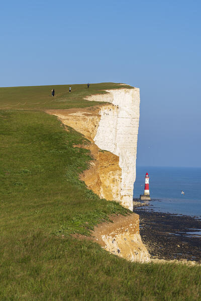 View of Beachy Head lighthouse with hikers walking along the cliff top, Seven Sisters Country Park, South Downs National Park, Sussex, England, United Kingdom, Europe
