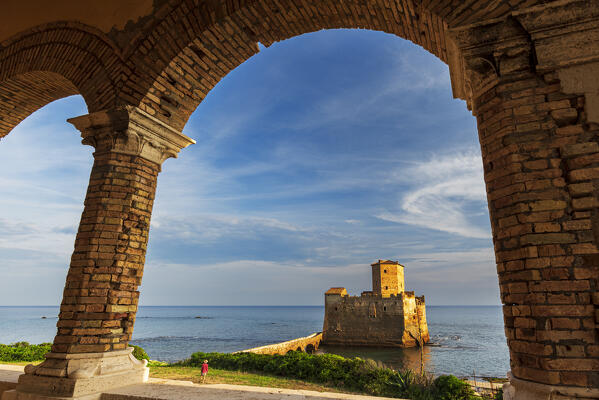 Man in green field admires the medieval castle of Torre Astura at sunset, Nettuno municipality, Rome province, Latium, Tyrrhenian sea, Italy, Europe (MR)