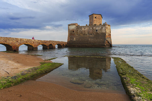 Fisherman walking to the castle of Torre Astura with reflection of the medieval tower in the water of the Tyrrhenian sea, Nettuno municipality, Rome province, Latium, Italy, Europe