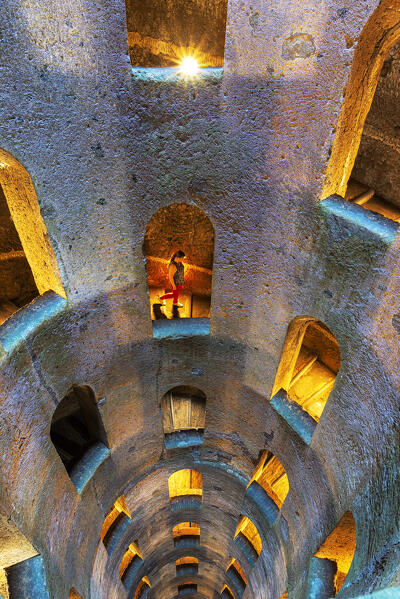 Woman descending the illuminated spiral staircase to the bottom of Saint Patrick well, Orvieto, Terni municipality, Umbria region, middle Italy, Italy, Europe (MR)