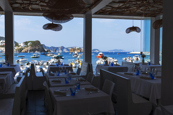 View of boats and rugged coast from a summer cafe in front of the blue waters of the marina of Ponza island, Pontine archipelago, Latina province, Latium region, Tyrrhenian Sea, Italy, Europe
