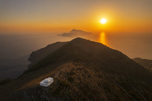 Aerial view of the white church of San Costanzo on top of a hill surrounding the Tyrrhenian sea with the island of Capri on the horizon, sunset view, Punta Campanella, Ieranto bay, Nerano, Massa Lubrense municipality, Amalfi coast, Naples province, Campania region, Tyrrhenian sea, Italy