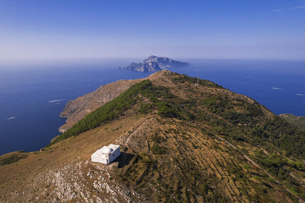 Small white church overlooking the Mediterranean sea standing on top of the mountain of the famous Amalfi coast with Capri island in the background, Punta Campanella, Ieranto bay, Nerano, Massa Lubrense municipality, Amalfi coast, Naples province, Campania region, Tyrrhenian sea, Italy