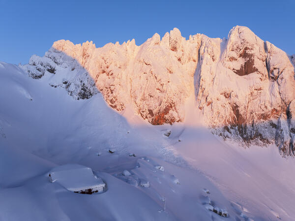 Sunrise over snowy Corno Piccolo with Carlo Franchetti hut in tick snow in the foreground, aerial view, Gran Sasso e Monti della Laga national park, Pietracamela, Teramo, Abruzzo, Apennines, Italy