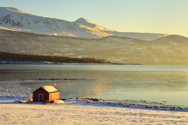 Wooden hut in the snowy landscape facing the cold sea on the road leading from Gibostad to Finnsnes Senja Tromso Norway Europe