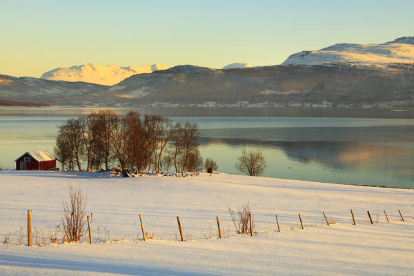 Wooden hut in the snowy landscape facing the cold sea on the road leading from Gibostad to Finnsnes Senja Tromso Norway Europe