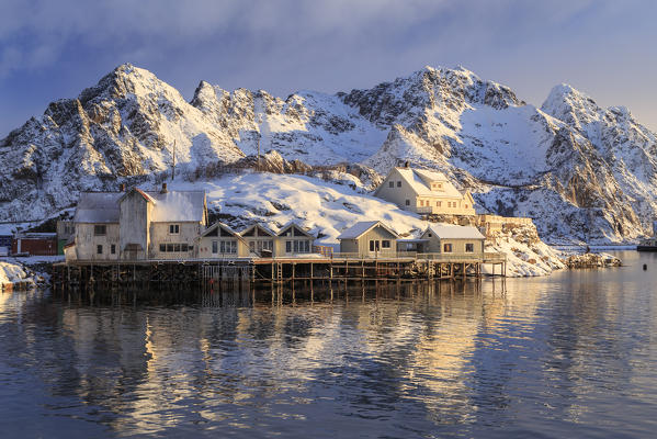 Stilt houses perched over the water in front of the stunning mountains of Henningsvær Fishing village, Lofoten Islands, Norway