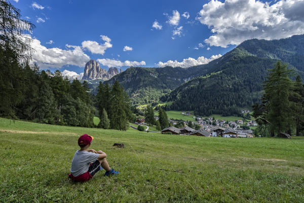 Child resting in front of the town of Ortisei with Sassolungo (Langkofel) on the back, Gardena Valley, Dolomites, Sudtirol, Italy