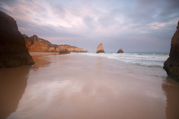  Sunset on cliffs and sandy beach surrounded by the clear sea Praia Dos Tres Irmaos Portimao Algarve Portugal Europe