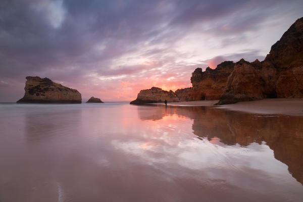 Sunset on cliffs and sandy beach surrounded by the clear sea Praia Dos Tres Irmaos Portimao Algarve Portugal Europe