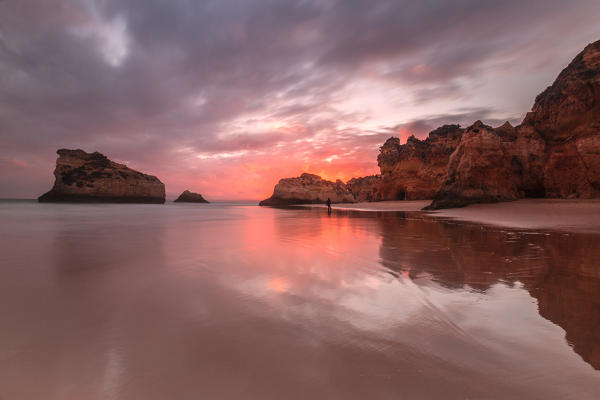  Sunset on cliffs and sandy beach surrounded by the clear sea Praia Dos Tres Irmaos Portimao Algarve Portugal Europe