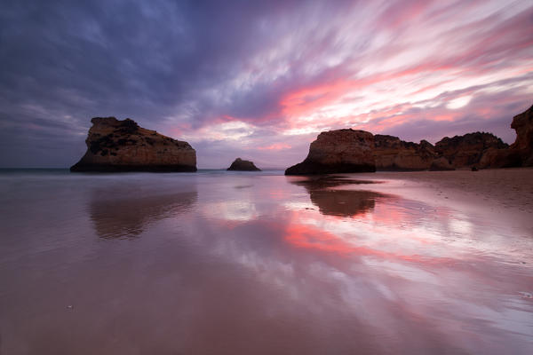  Sunset on cliffs and sandy beach surrounded by the clear sea Praia Dos Tres Irmaos Portimao Algarve Portugal Europe