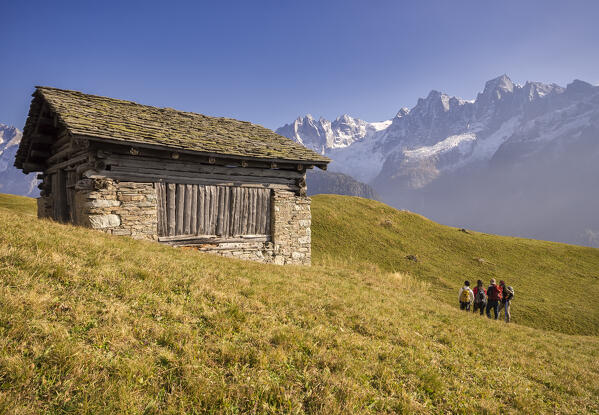 Hikers admire near a tipical alpine hut ,a snowy peaks of  Piz Cengalo and Badile, Tombal, Soglio, Val Bregaglia, canton of Graubunden Switzerland