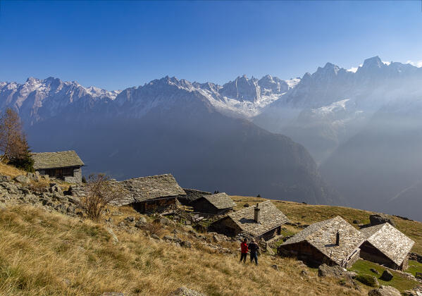 Hikers admire near a tipical alpine huts ,a snowy peaks of  Piz Cengalo and Badile, Tombal, Soglio, Val Bregaglia, canton of Graubunden Switzerland