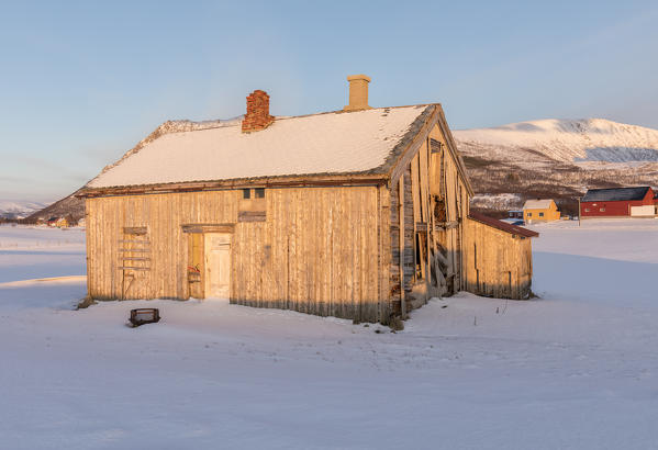 Old farm in wood  framed wooden huts called Rorbu and 
snowy peaks in the municipality of Andøy Vesterålen district of Nordland county Norway Europe