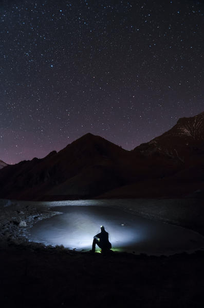 Hiker is looking a little alpine lake frozen (Soana Valley, Gran Paradiso National Park, Piedmont, Italy)
