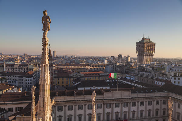 Milan, Lombardy, Italy. View of Velasca tower from the roof of Cathedral's Milan at sunset. In foreground there is a statue