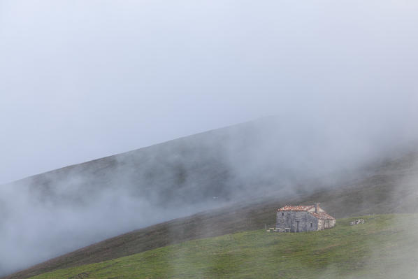 Pizzoc mountain, Cansiglio plateau, Veneto, Italy. A old farmhouse in the fog on Pizzoc mountain