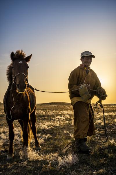 Mongolian shepherd wearing traditional dress in steppe of Gobi desert with his hourse, Mongolia, Mongolian, Asia, Asian.
