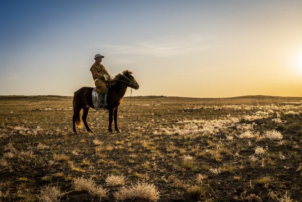 Mongolian shepherd wearing traditional dress in steppe of Gobi desert with his hourse, Mongolia, Mongolian, Asia, Asian.