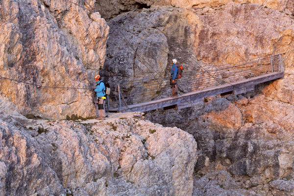 Europe, Italy, Veneto, Belluno. Two hikers on the suspended bridge with steel cables along the Kaiserjaeger trail, Lagazuoi, Dolomites