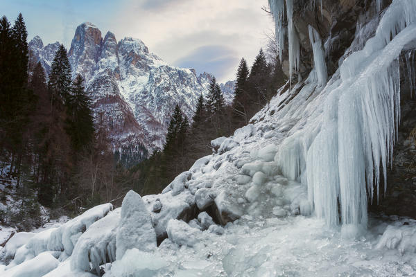 Ice stalagmites at the Inferno waterfall, in the background the Agner. The Cascata dell'Inferno (Hell waterfall), enclosed by cyclopean structures of Agner, Pale di San Lucano and the Pale of balconies (Pale di San Martino) at the bottom of the Valley of San Lucano. In winter, the ice is the king, creating a scenery worthy of the great north. Dolomites
