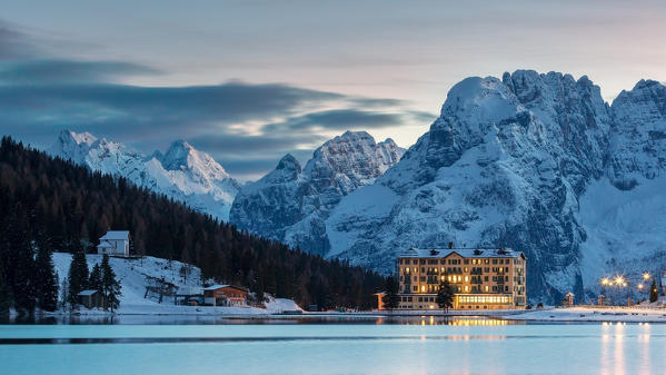 Dusk in Misurina, Auronzo, Dolomites, Veneto, Italy. Winter landscape with frozen lake and the silhouette of Sorapiss in the background.
