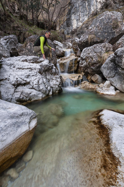 Hiker looking at the small waterfalls of turquoise water in val Salet, Monti del Sole, National park Belluno Dolomites, Italy