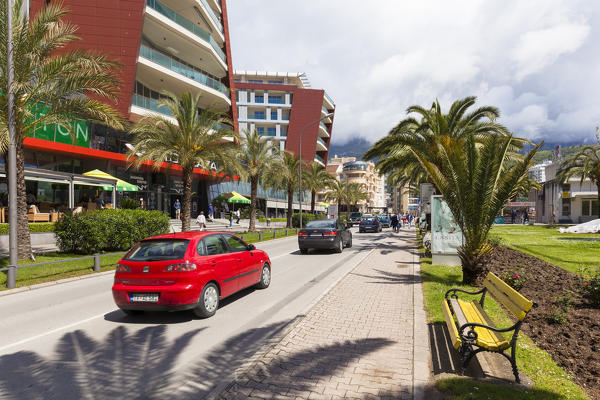 A street in Budva, car in transit between modern buildings and palm trees, Montenegro