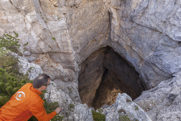 Europe, North Italy, Veneto, Belluno, Monti del Sole, Dolomites. Hiker leans over on the edge of the impressive Bus de le neole (hole of the clouds)