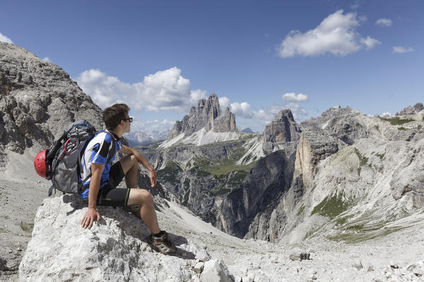 Europe, Italy, Veneto, Belluno. Hiker sitting on a rock looking the landscape towards Tre Cime di Lavaredo, Dolomites