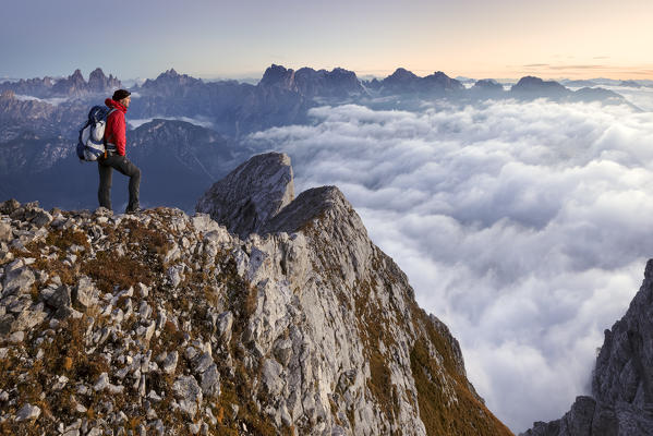 Europe, Italy, Veneto, Cadore, Auronzo. Hiker at dawn on the top of Cima dei Camosci, Marmarole, Dolomites, with sea of clouds in the valley