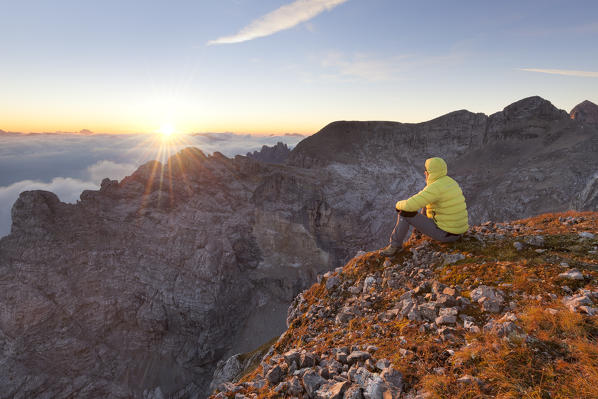 Europe, Italy, Veneto, Cadore, Auronzo. From Cima dei Camosci, Marmarole, Dolomites. a hiker is looking the rising sun