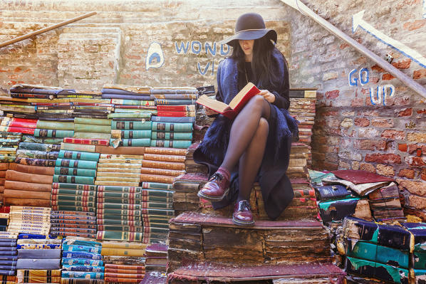 woman reading sitting on the staircase of books in the library Acqua Alta, Sestiere Castello, Venice, Veneto, Italy