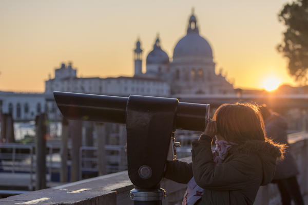 Little girl looking trough the telescope the Grand Canal, in the background the basilica di Santa Maria della Salute, Saint Mary of Health at sunset, Venice, Veneto, Italy