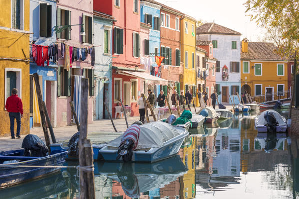 a lively street of burano, the colorful houses overlook the canal and people walk, Burano island, Venice, Veneto, Italy
