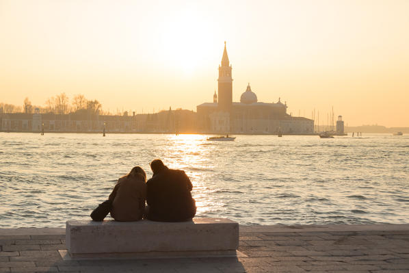 Couple of tourists admire the sunset towards the island of San Giorgio maggiore from the banks of the Grand Canal, Venice, Veneto, Italy