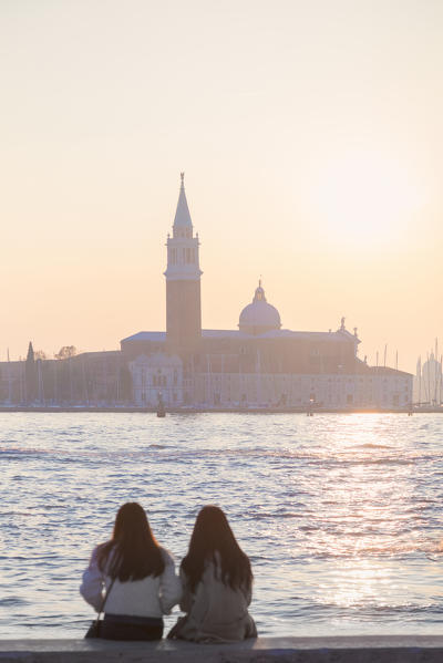 two tourists admire the sunset towards the island of San Giorgio maggiore from the banks of the Grand Canal, Venice, Veneto, Italy